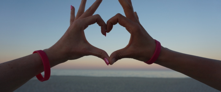Hände von zwei LAUFMAMAs formen ein Herz am Strand